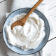 Im Bild ist eine blaue Schale Kokosjoghurt mit einem Kochlöffel aus Holz auf weissem Hintergrund.