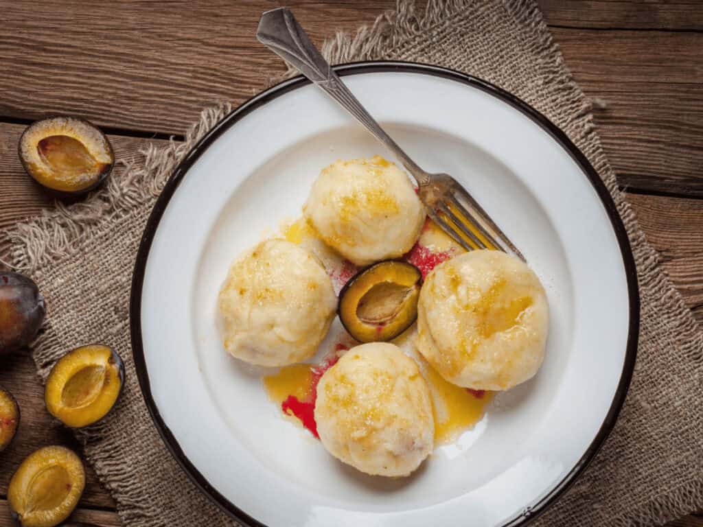 Gekochte Zwetschgenknödel auf einem weißen Teller mit dunklem Rand.
