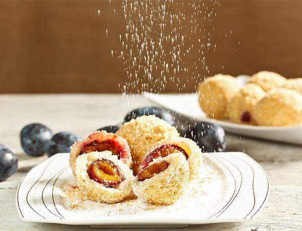 Zwetschgenknödel aus Süsskartoffeln im Bild auf einem weissen Teller mit Zucker-Zimt rieseln von oben.