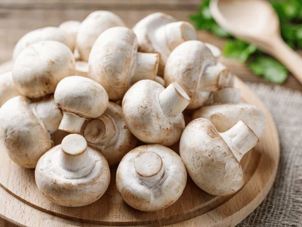Champignons auf einem Holzteller. Daraus werden gefüllte Champignons.
