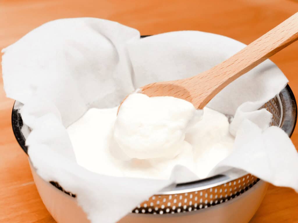 Joghurt tropft durch ein Tuch ab, daraus wird ein histaminarmer AIP-Frischkäse
