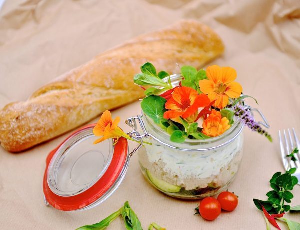 Eine Zucchini-Hirse-Bowl schön angerichtet im Glas mit Wildblumen und Baguette daneben liegend.