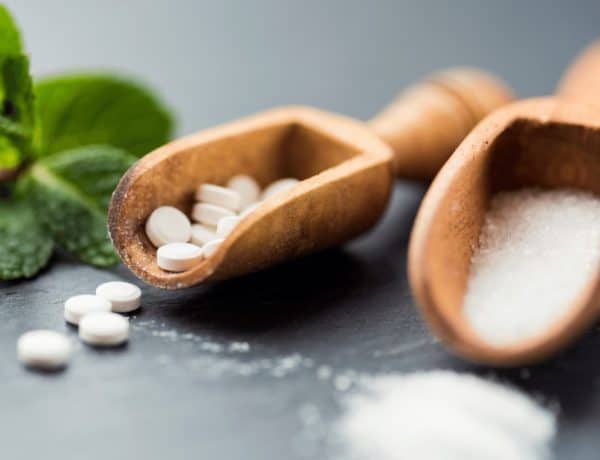 Zum Thema Süßstoffe beeinflussen den Blutzuckerspiegel: Stevia in Tabletten und Rieselform in Holzlöffeln und eine Steviapflanze