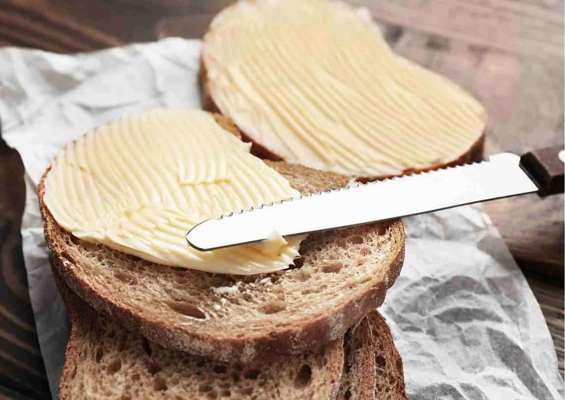 Ökotest Butter: zwei Scheiben Brot mit Butter, auf einem liegt ein Messer zum Verstreichen.