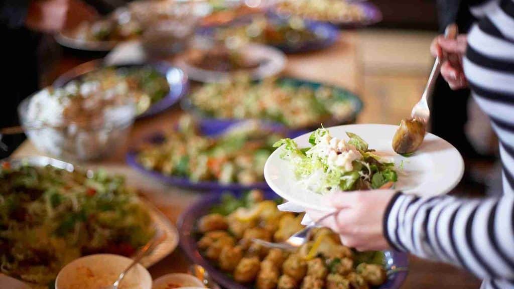 Glutenfreie Weihnachtszeit: Im Bild sind zwei Hände, die sich an einem Buffet einer Weihnachtsfeier bedienen.