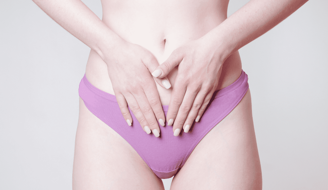 Eine Frau in hellviolettem Höschen legt beide Hände auf den Unterbauch Richtung Vulva (zum Thema Vulvodynie).