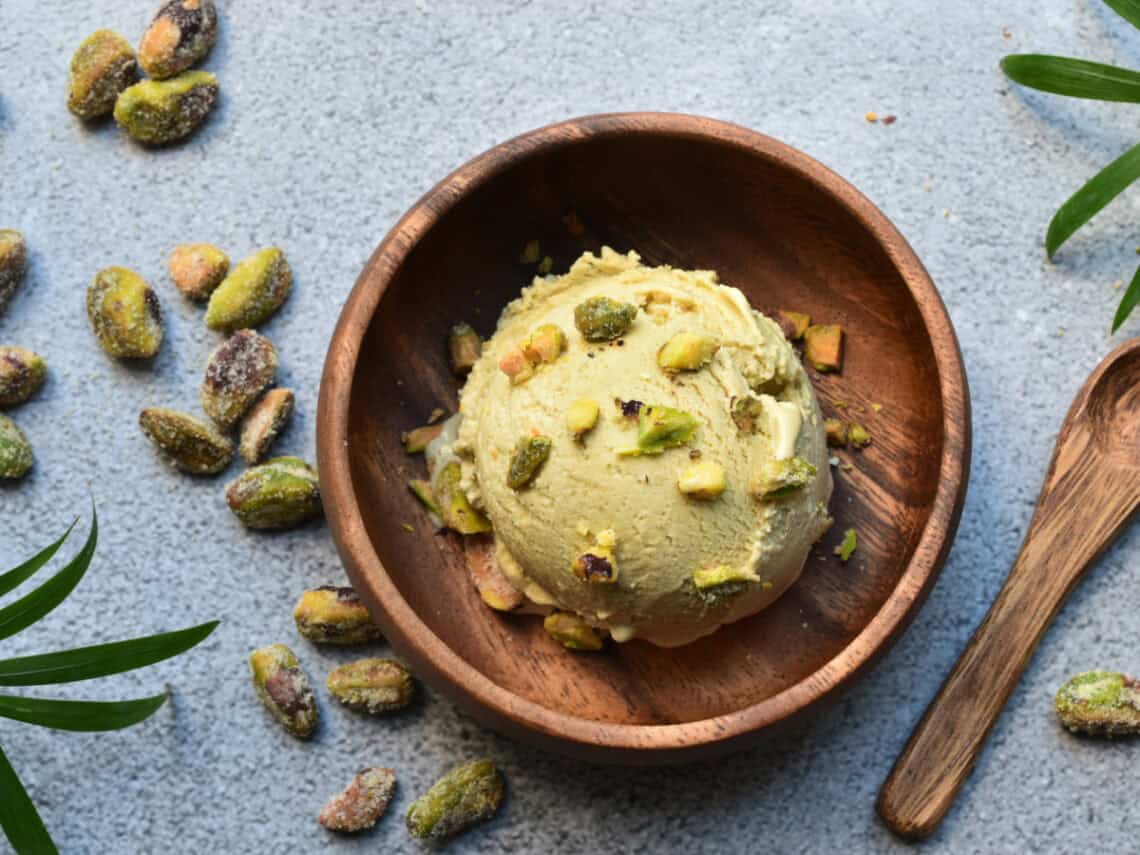 Eine kugel histaminarmes, veganes Pistazieneis in einer Holzschale, getoppt mit frischen Pistazien.