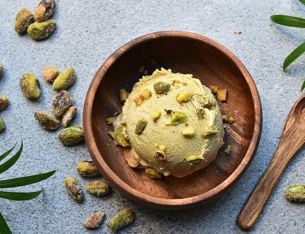 Eine kugel histaminarmes, veganes Pistazieneis in einer Holzschale, getoppt mit frischen Pistazien.