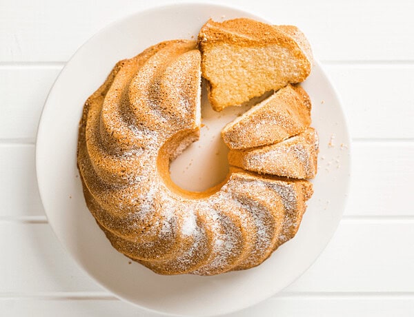 Glutenfreier, histaminarmer Gâteau de Savoie auf einem weißen Teller, ein Stück liegt auf der Seite.