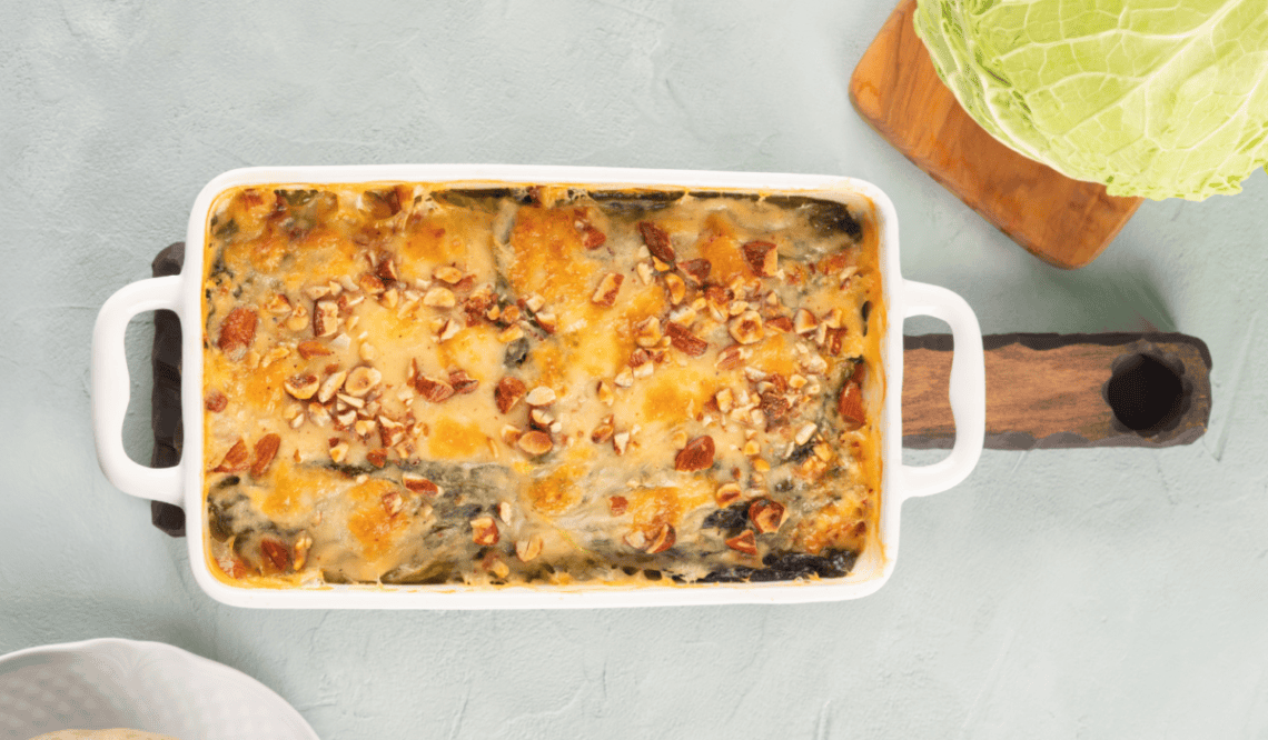 Süßkartoffel-Kohl-Auflauf in einer weißen Auflaufform, im Hintergrund ein Kohlkopf.