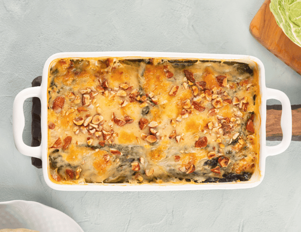 Süßkartoffel-Kohl-Auflauf in einer weißen Auflaufform, im Hintergrund ein Kohlkopf.