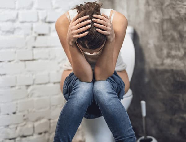 Eine Frau sitzt völlig fertig auf der Toilette. Symbolbil zum Thema Mastzellen, Histamin und Reizdarm.